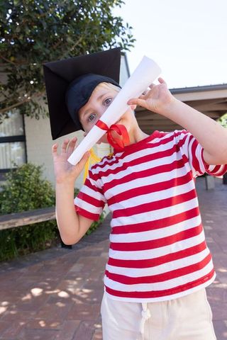 Boy wearing mortarboard and holding diploma on brick patio celebrating school graduation