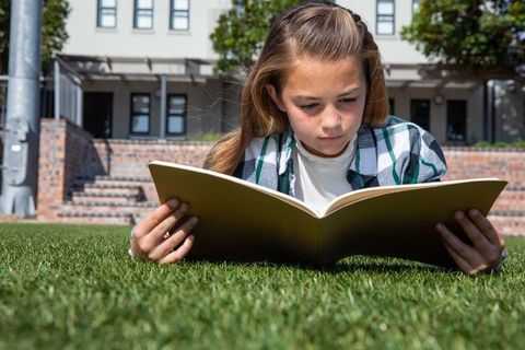 Young Girl Outdoors Reading Large Book on Sunny Day
