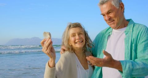 Joyful senior couple holding seashell on sunny beach day