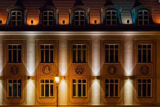 This photo showcases an illuminated building facade at night with intricate architectural details. The streetlamp adds a creative light source that emphasizes the structure’s beautiful design. This image can be used in projects related to architecture, urban environments, downtown in the evening, and historical buildings.