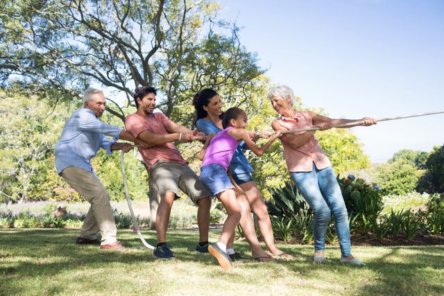 Multigenerational family enjoying a fun game of tug of war in a park. Ideal for promoting family bonding, outdoor activities, and healthy lifestyles. Perfect for advertisements, family-oriented content, and community events.
