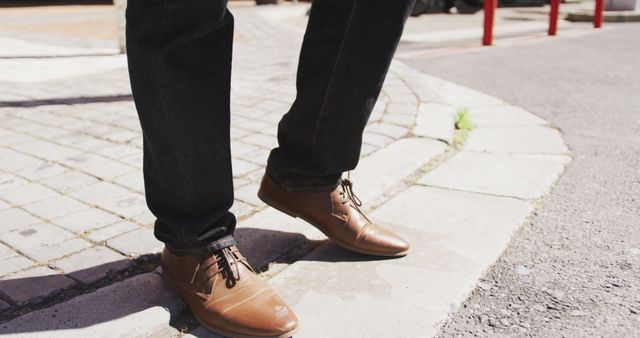 This scene portrays a man walking on a city sidewalk, capturing a close-up of his stylish leather shoes and jeans. Excellent for use in fashion-related materials, particularly for showcasing men's footwear, casual city life, or urban fashion trends.