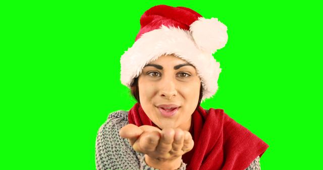 This image showing a woman wearing a Santa hat and blowing a kiss against a green screen background is ideal for holiday and Christmas-themed content. It can be used for creating festive greeting cards, social media holiday messages, winter season campaigns, and promotional materials emphasizing warmth and celebration. The green screen background allows easy integration into various designs.