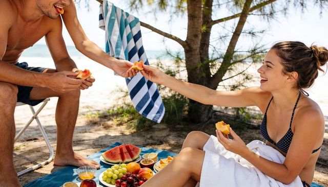 Couple sharing fresh fruit on beach picnic under tree summer sunlit relaxation and romance