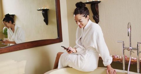 Happy woman in bathrobe enjoying self-care with a smartphone