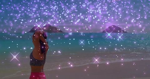 Woman stretching on tropical beach facing ocean with purple sparkle bokeh overlay
