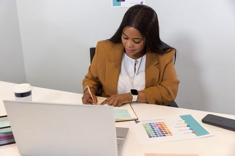 African american professional woman taking notes at laptop with color palette and smartwatch