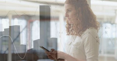 Female analyst holding smartphone with data visualization overlay in open-plan office