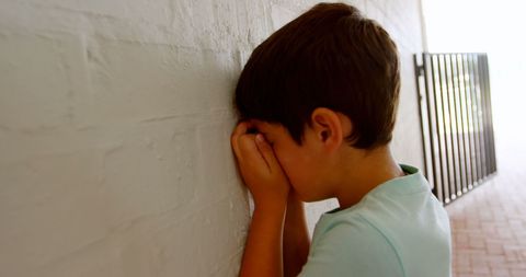 Young Boy Leaning on Wall with Hands over Face