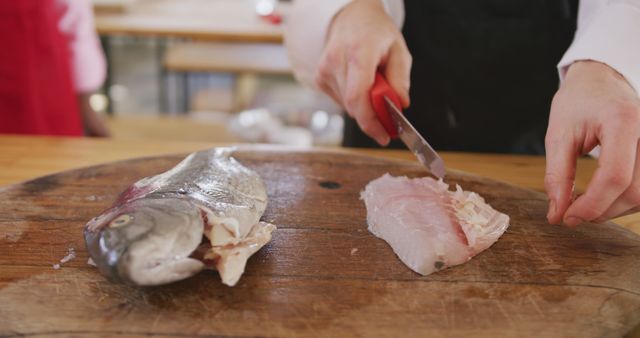 Hands of caucasian female cook slicing fish on cutting board in kitchen. Lifestyle, food, cooking and senior lifestyle, unaltered.