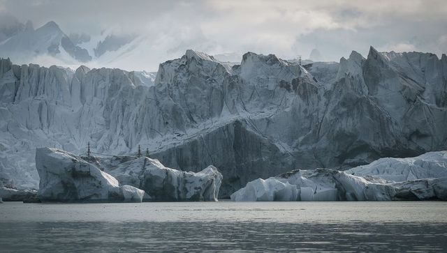 Massive glacial ice cliff towering over calm fjord with icebergs and utility cables