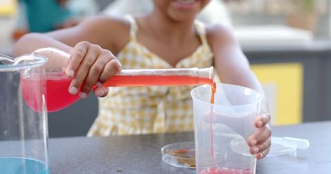 Enthusiastic girl pouring red liquid in classroom science experiment