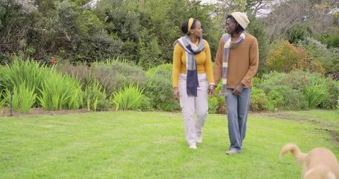 African american couple walking hand in hand on green lawn wearing scarves and beanie