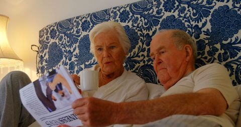 Senior Couple Reading Newspaper in Bedroom