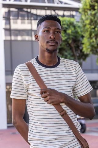 African american man standing in downtown plaza holding crossbody strap and looking upward