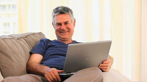 Mature Man Relaxing with Laptop on Sofa at Home