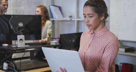 Focused professional woman reading on laptop while checking world map on office monitor