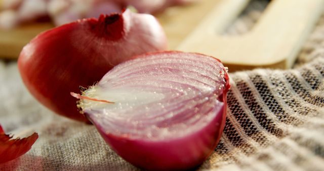 Red onion half and one whole onion placed on a striped cloth. This close-up shot highlights the texture and freshness of the vegetables, making it perfect for use in food blogs, recipe books, or culinary websites. Can also be used in articles focusing on healthy eating, ingredient preparation, or kitchen techniques.