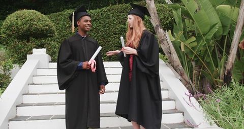 Diverse graduates celebrating on outdoor steps wearing caps and gowns holding diplomas