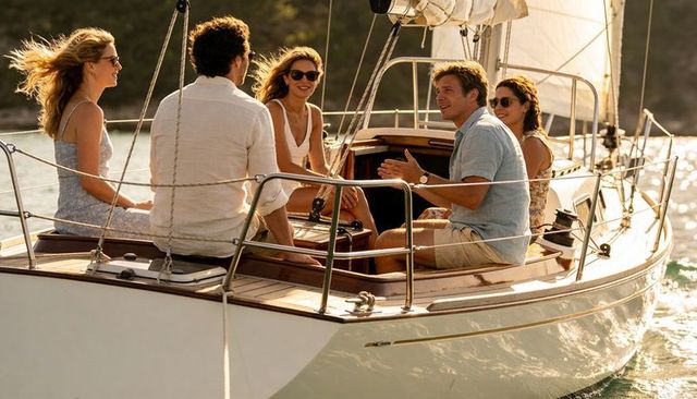 Friends chatting during golden-hour sail on luxury yacht near tree-lined coastline