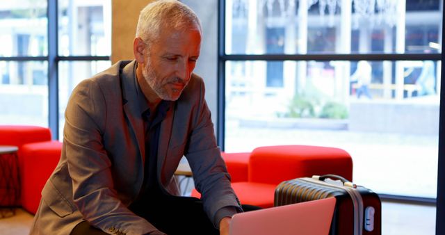 Middle-aged businessman using laptop in modern office lobby - Download Free Stock Images Pikwizard.com