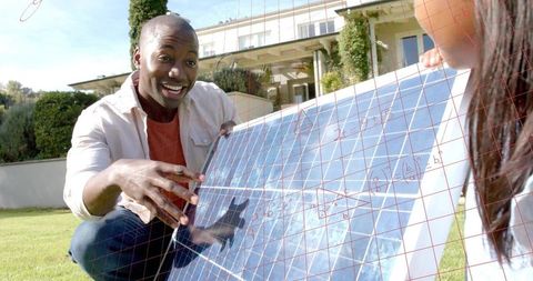 Kneeling man demonstrating residential solar panel installation on lawn with enthusiastic smile