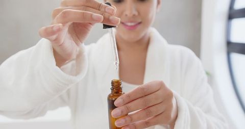Asian Woman Applying Serum from Amber Bottle During Skincare Routine
