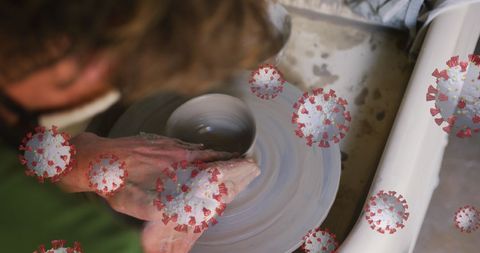 This creative visual mixes the hands of an artisan shaping clay on a pottery wheel with graphics of the COVID-19 virus. It can symbolize the tension between human creativity and the pandemic. Useful for articles or features examining the impact of COVID-19 on artisanal practices or during workshops promoting safety and adaptability in creative spaces.
