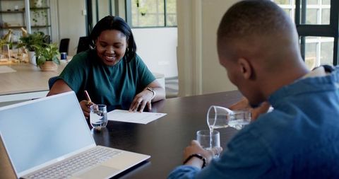 African colleagues signing document while coworker pouring water in modern office meeting