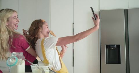 Friends taking selfie in kitchen while baking and laughing
