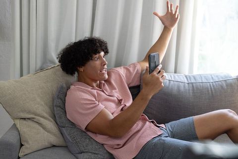 Young man reacting to smartphone while lounging on sofa, raising arm in excitement
