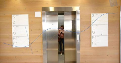 Woman holding phone reflecting in elevator gap wood-paneled lobby with signage