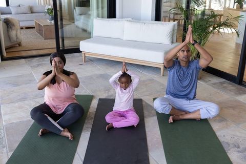 Diverse family practicing meditation and yoga on home patio with child in lotus pose