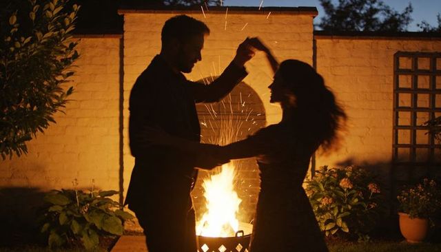 Dancing couple silhouetted by backyard fire pit at dusk, romantic outdoor evening scene