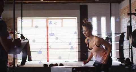 Female athlete performing plyo box jumps in boxing gym with coach holding clipboard