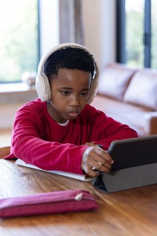 African american boy learning on tablet with headphones at home studying remotely