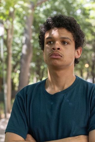 African american man 20s standing with arms crossed under dappled leafy canopy