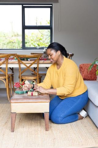 African american woman wrapping gifts in cozy living room with festive decor and natural light