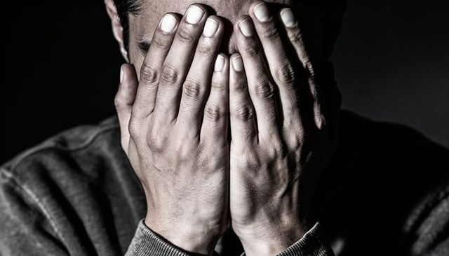 Light-skinned man covering face with hands, dramatic low-key portrait showing distress