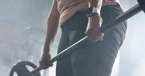 Mid-adult woman holding loaded barbell wearing smartwatch and leggings strength training