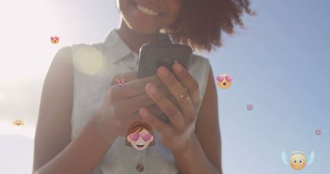 Smiling Woman with Smartphone Surrounded by Emoticons Outdoors