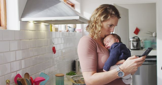 Multitasking Mother Holding Newborn Baby While Checking Phone in Kitchen - Download Free Stock Images Pikwizard.com