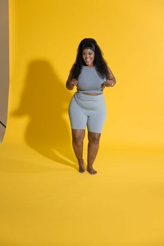 Smiling african-american woman in gray activewear barefoot on vibrant yellow background