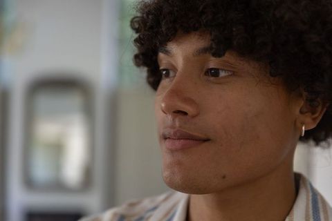 Thoughtful young man gazing left wearing hoop earring and striped shirt indoor headshot