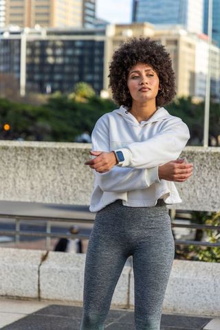 African american woman stretching on urban plaza at golden hour wearing hoodie and leggings