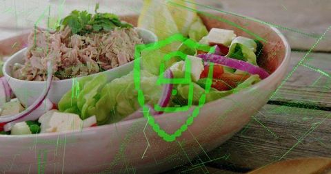 Tuna salad with feta and cucumber in pastel pink bowl on wooden table with green overlay