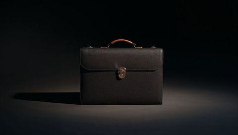 Featuring dark pebbled leather briefcase with brass lock under low-key lighting