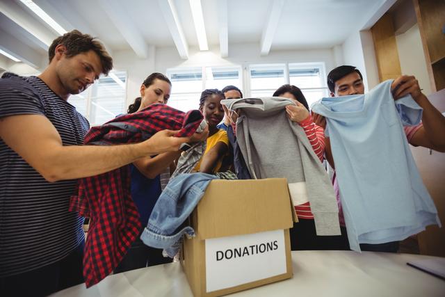 Group of volunteers sorting and organizing clothes for donation. Ideal for use in articles, blogs, and promotional materials related to charity work, community service, and nonprofit organizations. Highlights themes of teamwork, social responsibility, and humanitarian aid.