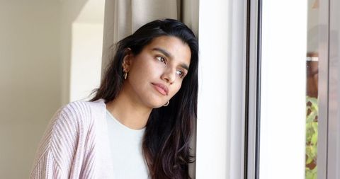 Contemplative Woman Leaning Against Window in Cozy Home