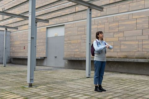 Asian woman checking wristwatch in urban courtyard with backpack and denim jacket